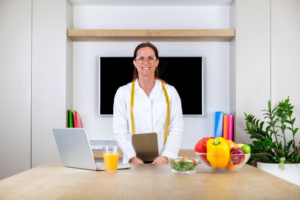 一个微笑的年轻女医生的肖像，营养师站在明亮的现代办公室的秤和卷尺图片下载