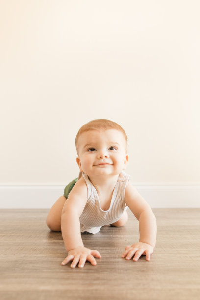一名7个月大的患有多指畸形的大男婴，穿着橄榄绿可重复使用和可持续的布料尿布和米色背心，正在家里的木地板上学习爬行图片下载