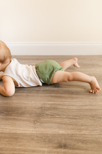 2022年，患有多指畸形的7个月大的大流行男婴，穿着橄榄绿颜色的可重复使用和可持续的布尿布，在家里的木地板上爬行，以下犬式和腹部躺着图片下载
