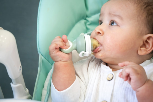 一个快乐满足的婴儿吃着奶头上的香蕉泥。引入辅食、宝宝健康食品，让宝宝在餐桌上进食图片下载