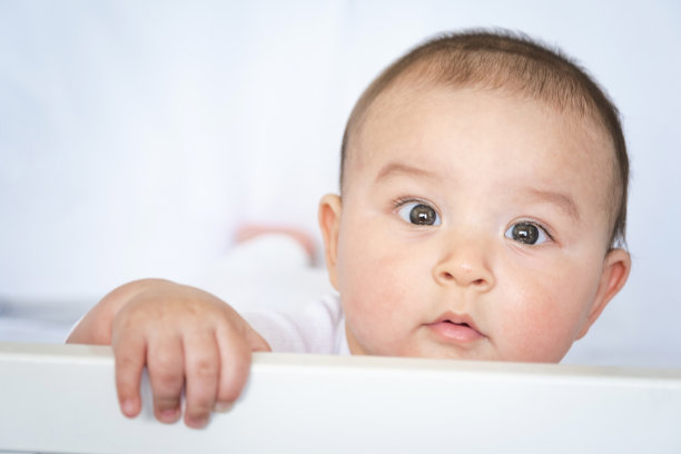 可爱的肖像婴儿在婴儿床的特写。一个穿白衣服穿白内衣的孩子。温柔和关怀，孩子的问题。图片下载