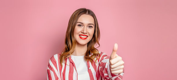 年轻女子在条纹衬衫显示像手势孤立在工作室的粉红色背景图片下载