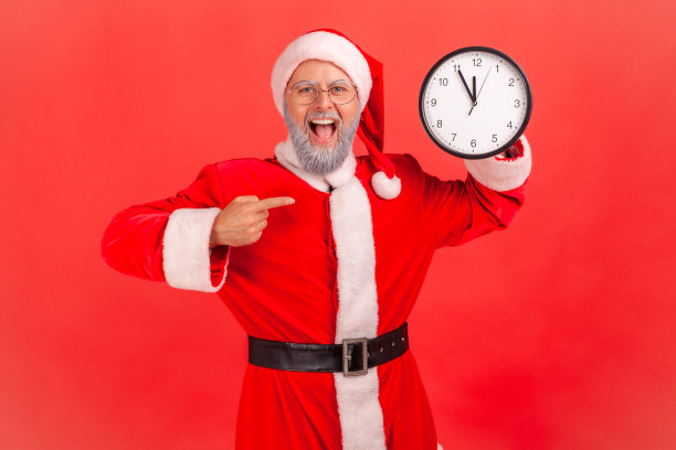 身穿圣诞老人服装、胡子花白的老人兴奋地指着挂钟，嘴巴张得大大的，表情令人惊叹。图片下载