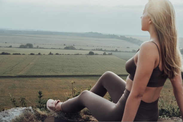 迷离的年轻女子坐在户外的山顶上，专注于日落的全景景观图片下载