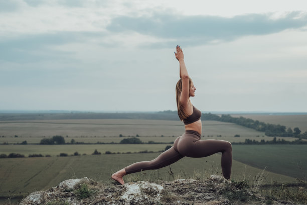 运动女孩在山顶做伸展运动，年轻女子在户外练习瑜伽，日落后的全景图片下载