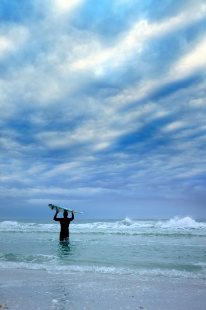 年轻人在暴风雨的海面上把冲浪板举过头顶图片下载