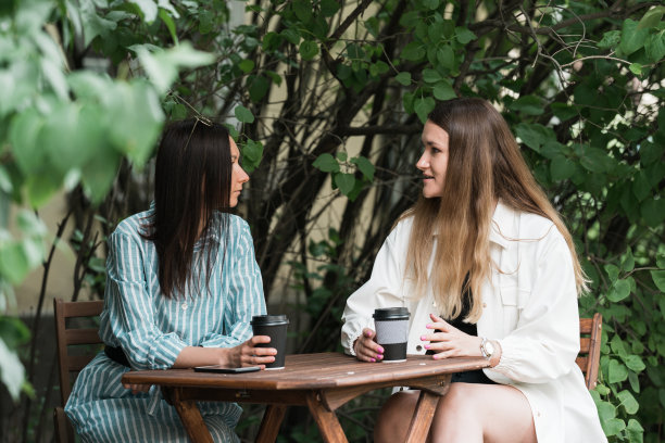 两名年轻女子坐在公园咖啡厅的偷拍照片。图片下载