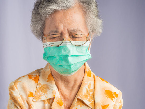 一位白发苍苍的老妇人的肖像，戴着面具，站在灰色的背景下向下看图片下载