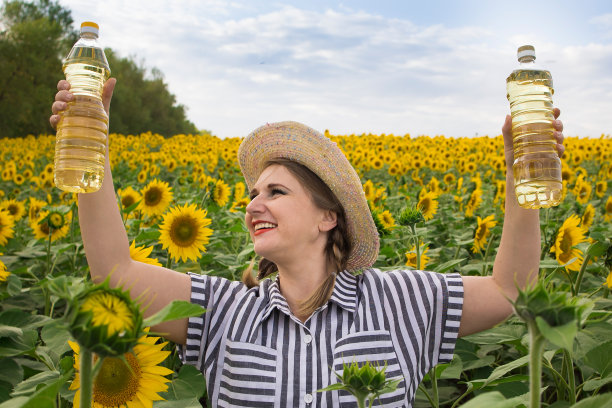 美丽微笑的中年农妇手里拿着金色的葵花籽油，在阳光灿烂的向日葵田图片下载