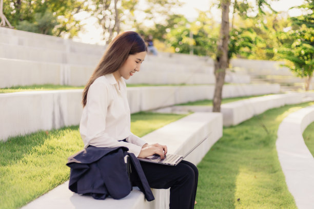亚洲美丽的女商人打字键盘，而坐在公园工作。图片下载