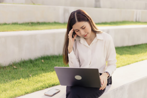 亚洲女商人坐在公园里用笔记本电脑工作感到焦虑。图片下载