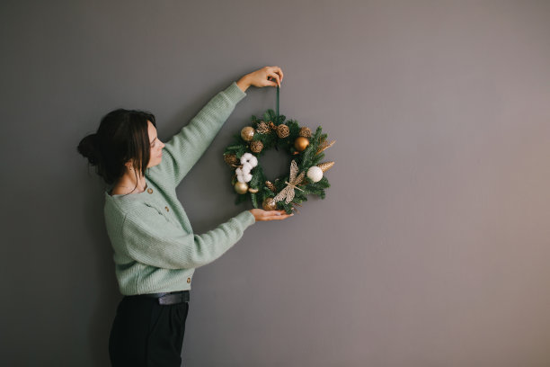 千禧一代女性用手工圣诞花环装饰灰色墙壁。喜庆的节日装饰。图片下载