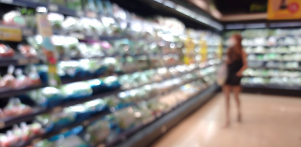 模糊的亚洲女性选择绿色产品在超市，水果和蔬菜区。杂货店内部的散焦视图。杂货店货架上陈列的一排农产品。图片下载
