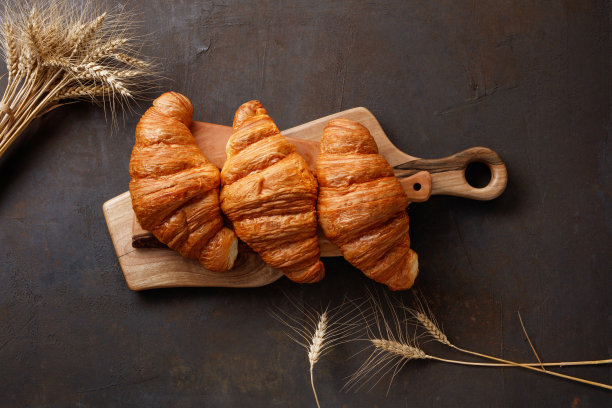 板和美味的羊角面包在黑暗的桌子上，小穗，接近。图片下载