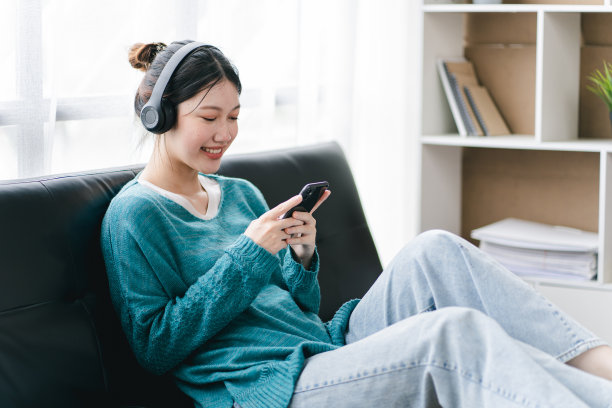 她正在用智能手机听音乐，戴着耳机。图片下载