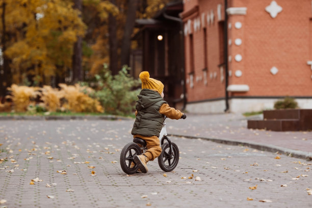 一个快乐的小男孩在户外骑自行车。一个快乐的孩子在秋天的公园里散步。婴儿穿着时髦的背心和工装裤。图片下载