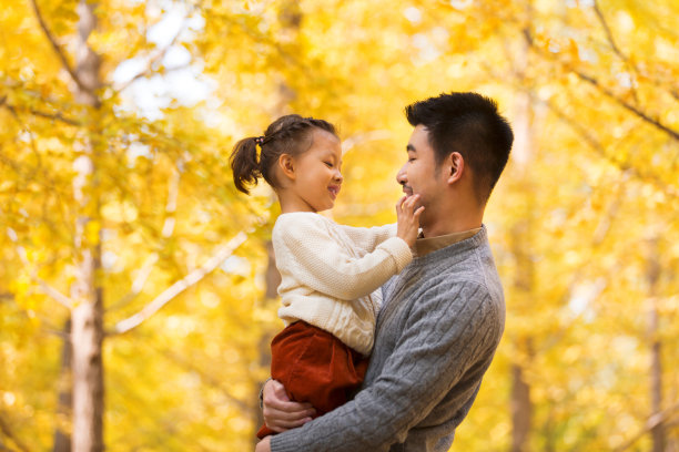 年轻的中国父亲抱着他的女儿在秋天的森林里，小女孩的手触摸着她父亲的胡渣照片图片下载