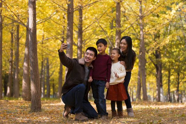 一家四口年轻的父母和孩子在秋天的树林里用手机自拍- stock photo图片下载