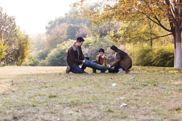 秋天，一家三口准备在树和草之间搭起户外露营帐篷-图片图片下载
