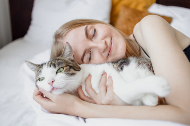 年轻的金发30多岁的女人抱着可爱的绿色眼睛虎斑猫的肖像。女性在早上睡觉时抱着猫图片下载