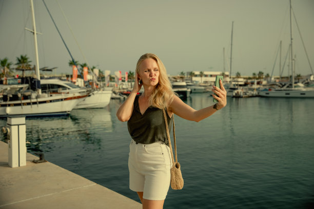 美丽的女人在蓝色的大海和游艇的背景下打电话图片下载