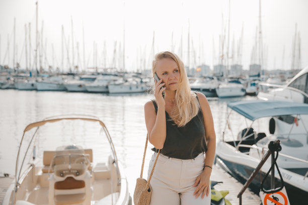 美丽的女人在蓝色的大海和游艇的背景下打电话图片下载