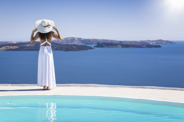 在圣托里尼岛，一名身着夏季连衣裙的女子看着火山口的景色图片下载
