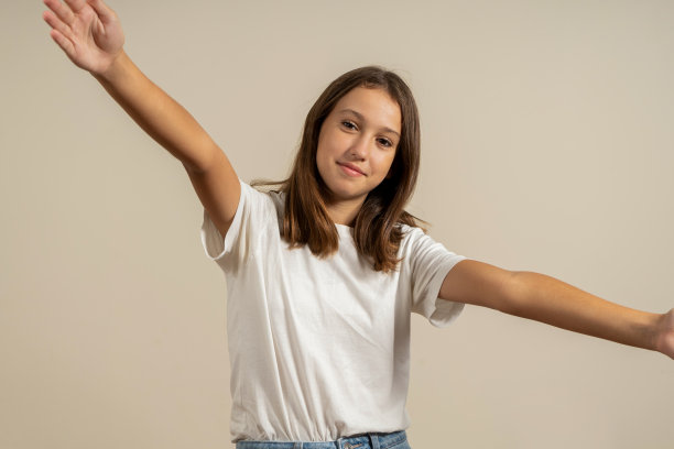 漂亮的西班牙十几岁的女孩与深色头发的拥抱的姿态，而微笑着对着镜头，孤立的米色背景。图片下载