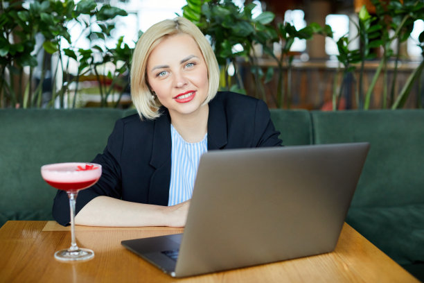 有灵感的迷人模特在她的笔记本电脑上写作，花时间独自在咖啡馆，在桌子上有一杯鸡尾酒，忙碌，穿着西装。图片下载