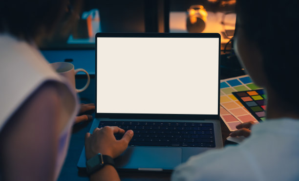 女商人晚上坐在办公室的桌子上，使用笔记本电脑，模拟一个黑屏，用于应用程序。图片下载