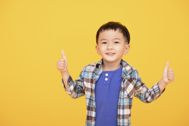 快乐的小男孩在黄色背景前竖起大拇指图片下载