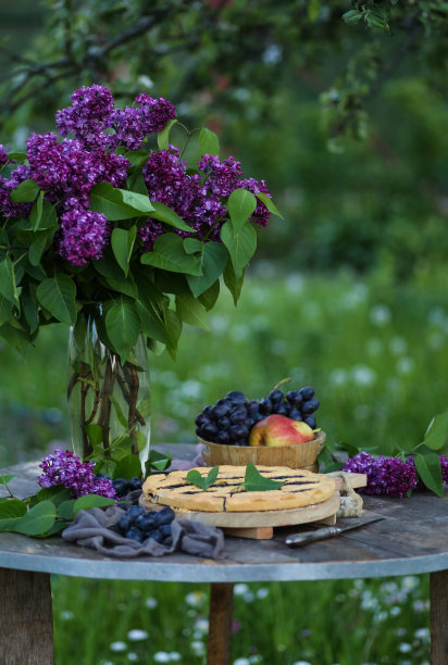 夏天的花园。花瓶里插着一束紫丁香，旧木桌上放着果酱蛋糕。新鲜水果和浆果，葡萄，梨。户外,太阳。乡村。背景图像，复制空间图片下载