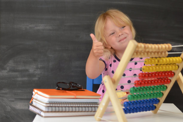 回到学校。里面一个有趣的小女孩正坐在一张桌子旁，背景是黑板。图片下载