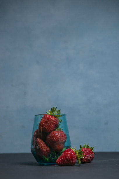 新鲜草莓在一个美丽的杯子里，深蓝色的背景。主音。有选择性的重点。大气夏天的背景，心情。广告夏季派对。夏季促销优惠。图片下载