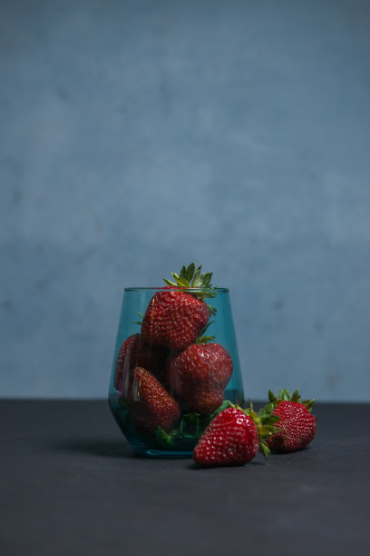 新鲜草莓在一个美丽的杯子里，深蓝色的背景。主音。有选择性的重点。大气夏天的背景，心情。广告夏季派对。夏季促销优惠。图片下载