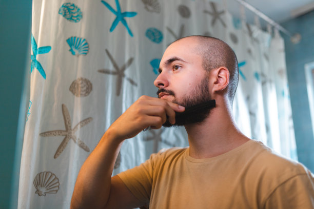 秃顶的年轻人在镜子前梳理他的胡子图片下载