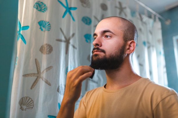 秃顶的年轻人在镜子前梳理他的胡子图片下载