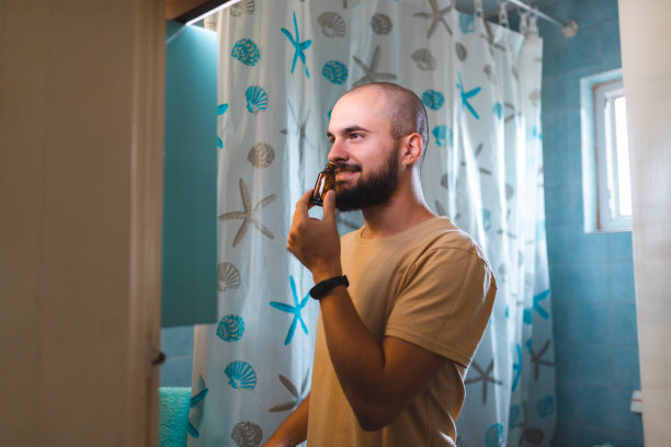 秃顶的年轻人在镜子前梳理他的胡子图片下载
