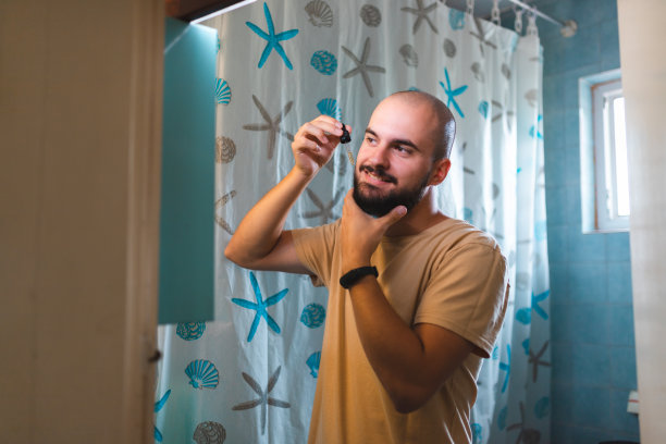 一个秃顶的年轻人对着浴室的镜子直接在胡子上涂胡子油图片下载
