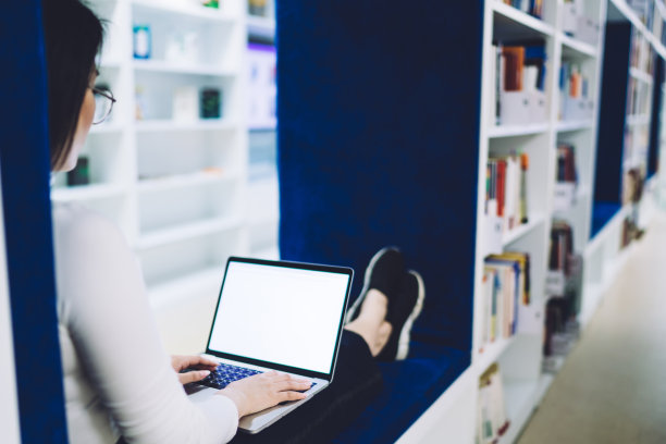 学生坐在图书馆的长凳上，注意力集中在屏幕上，与笔记本电脑互动图片下载