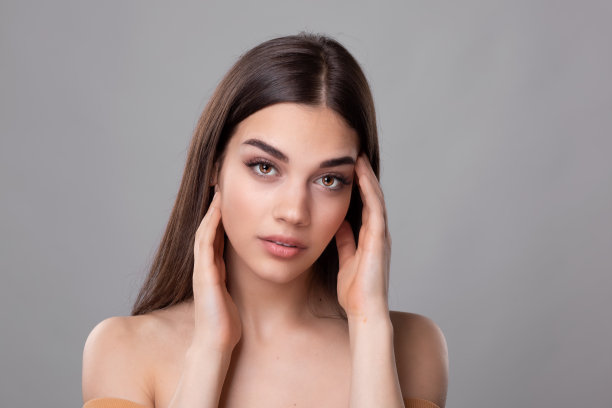 美丽的年轻女子有着干净完美的皮肤。美女模特的肖像与自然的化妆和触摸她的脸。水疗、护肤和健康。关闭,copyspace。库存图片图片下载