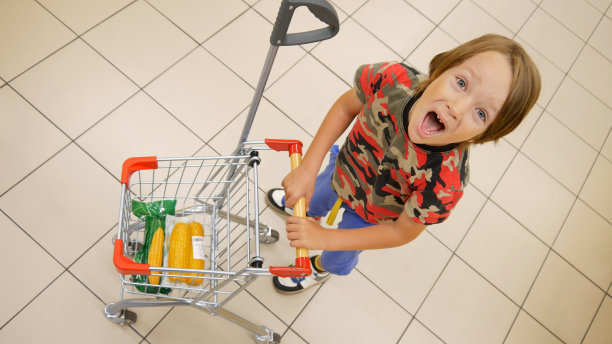 一个有趣的尖叫小男孩与一个小购物手推车的特写图片下载