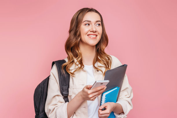 学生女孩微笑着看向别处，拿着一个智能手机隔离在粉红色的背景上图片下载