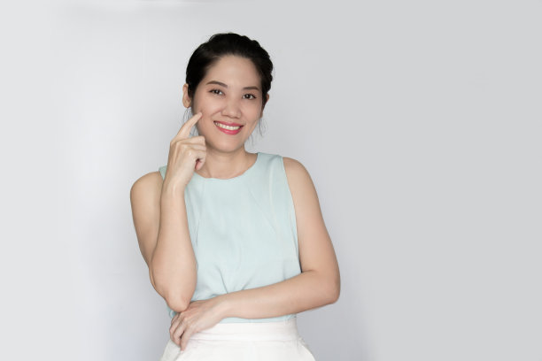 亚洲美女用手指在她的脸颊上，另一只胳膊交叉在腰上，微笑着幸福地拥有或得到新的想法或为她的皮肤感到自豪图片下载