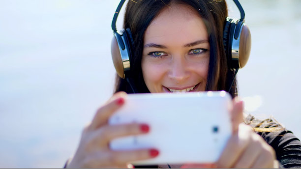 夏天，户外，一个美丽的女人的肖像，长着深色的头发，从手机上戴着耳机听音乐，设备，用手机拍摄视频，自拍。图片下载