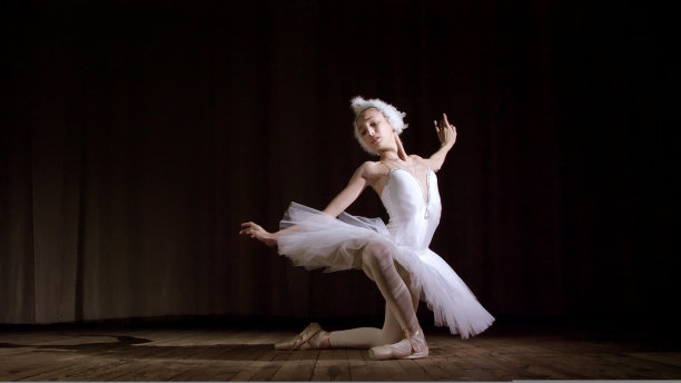 在聚光灯下，老剧院的舞台上。年轻的芭蕾舞演员穿着白天鹅装和尖头鞋，优雅地跳着某些芭蕾舞动作，部分不穿胸罩图片下载