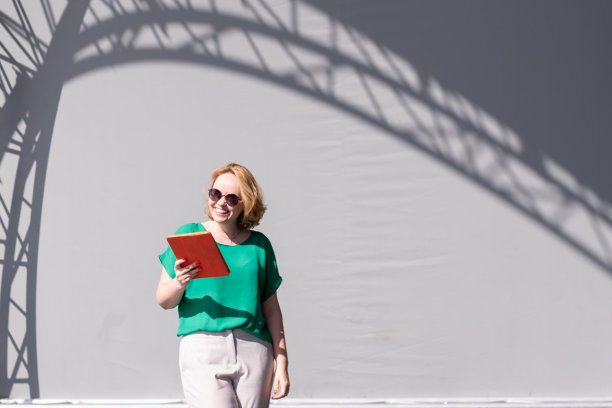快乐女孩戴着墨镜浏览平板电脑，倚在街边的墙上，美丽的身影。图片下载