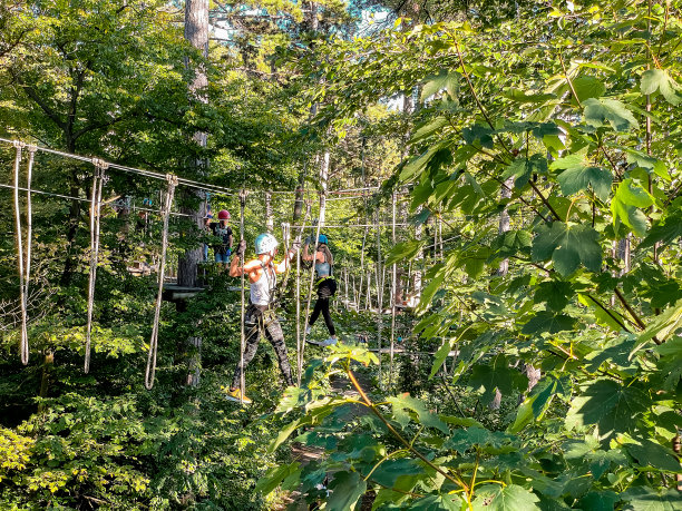 一名十几岁的女孩在游乐园的树木之间的索桥上走在安全装备和头盔。森林中的绳索公园。夏天的乐趣和体育冒险的人。快乐的女学生在一个夏天的登山冒险公园享受活动。图片下载