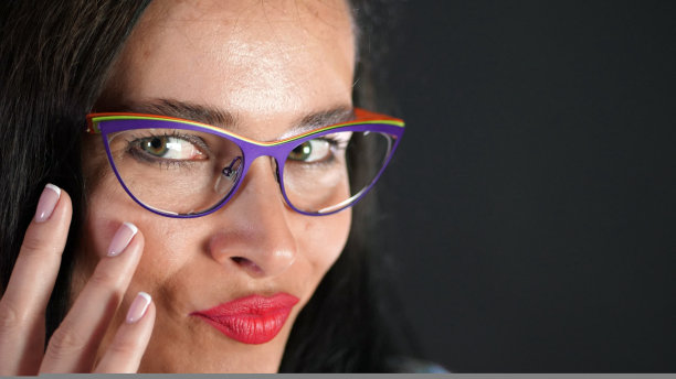 一个性感的黑发女人的肖像与红色的嘴唇谁色情和开玩笑地尝试时髦的眼镜，眼镜和在演播室性地看着镜头。黑暗的灰色背景。图片下载