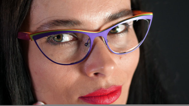 一个性感的黑发女人的肖像与红色的嘴唇谁色情和开玩笑地尝试时髦的眼镜，眼镜和在演播室性地看着镜头。黑暗的灰色背景。图片下载